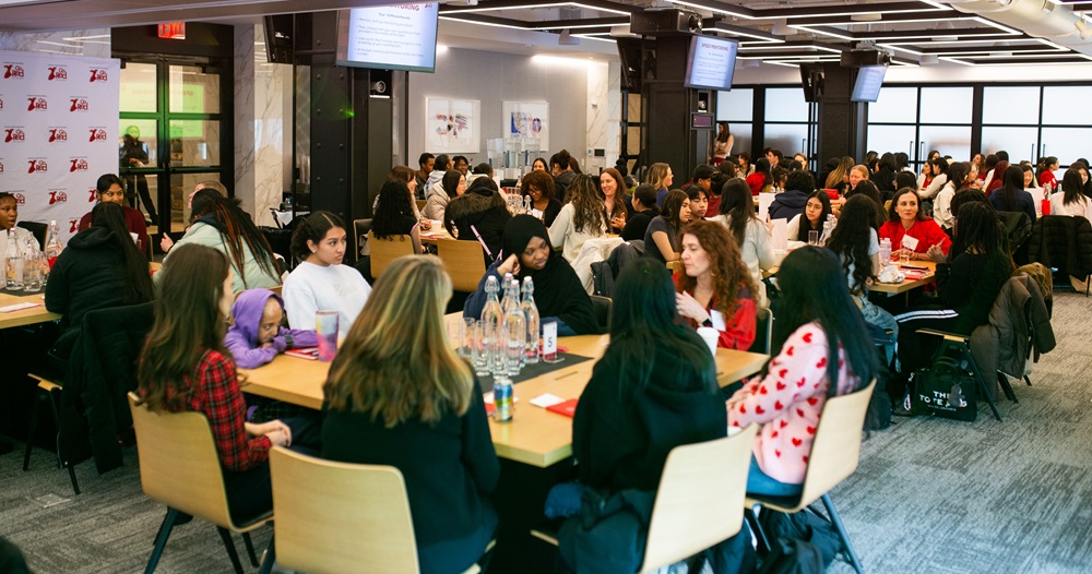 Large room with women seated around several tables having discussions.